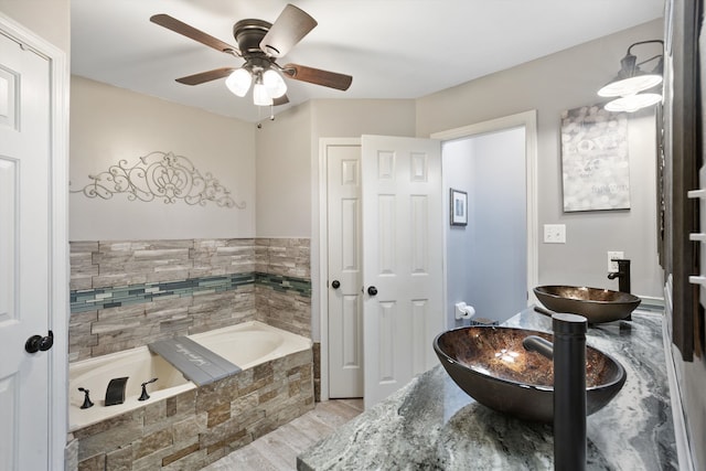 bathroom with vanity, a relaxing tiled tub, wood-type flooring, and ceiling fan