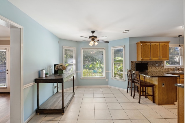 kitchen featuring light tile patterned flooring, a kitchen breakfast bar, ceiling fan, pendant lighting, and decorative backsplash