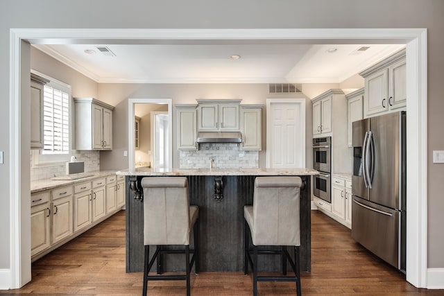 kitchen with a breakfast bar area, appliances with stainless steel finishes, a kitchen island, light stone countertops, and dark hardwood / wood-style floors