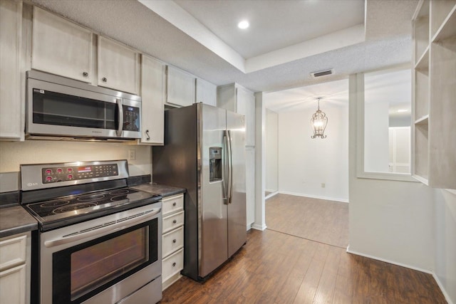 kitchen with dark wood-type flooring, stainless steel appliances, decorative light fixtures, a raised ceiling, and a textured ceiling