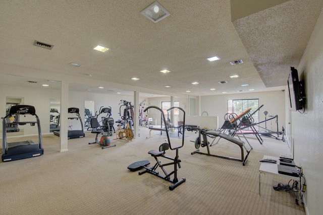 exercise room with light carpet and a textured ceiling