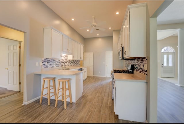 kitchen featuring decorative backsplash, white cabinetry, a kitchen bar, light hardwood / wood-style floors, and stainless steel appliances