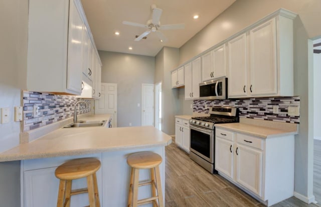 kitchen featuring appliances with stainless steel finishes, sink, light wood-type flooring, a kitchen breakfast bar, and white cabinets