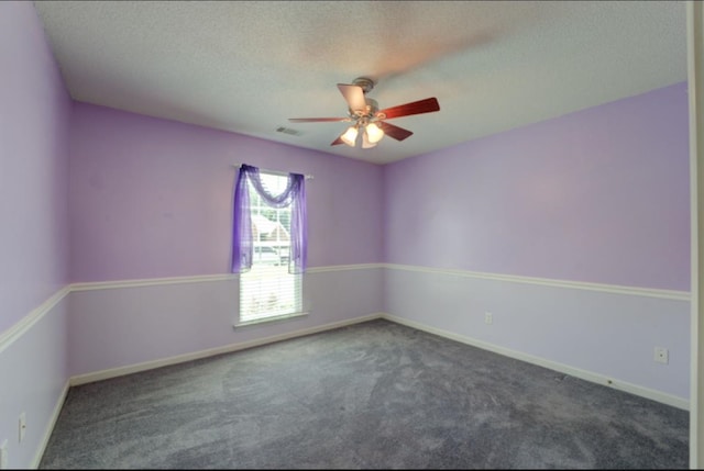 empty room featuring ceiling fan, a textured ceiling, and dark colored carpet