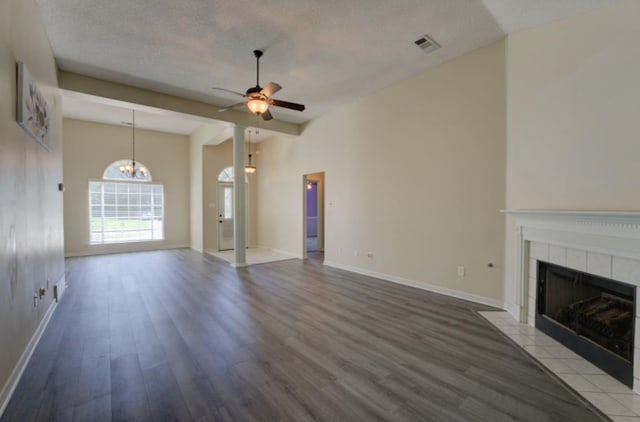 unfurnished living room featuring wood-type flooring, a textured ceiling, a tile fireplace, and ceiling fan with notable chandelier