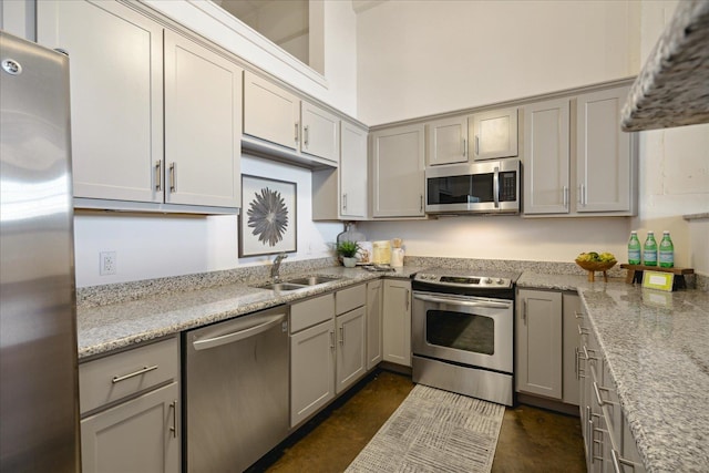 kitchen with gray cabinetry, sink, light stone counters, and stainless steel appliances