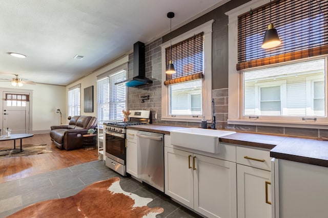 kitchen featuring wall chimney range hood, decorative light fixtures, appliances with stainless steel finishes, and dark hardwood / wood-style flooring