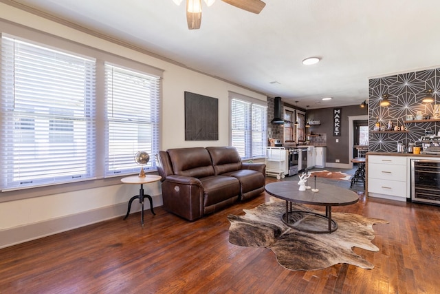 living room featuring wine cooler, ceiling fan, indoor bar, ornamental molding, and dark wood-type flooring