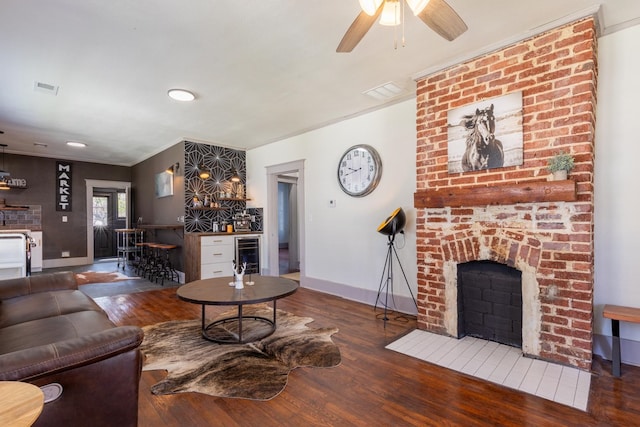 living room featuring dark wood-type flooring, wine cooler, bar, and a brick fireplace