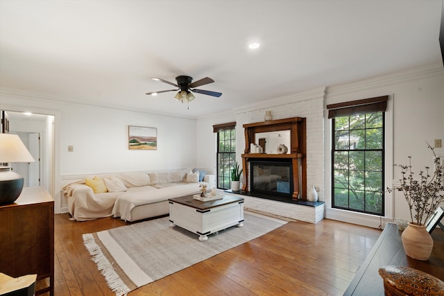 living room featuring crown molding, a brick fireplace, hardwood / wood-style flooring, and ceiling fan