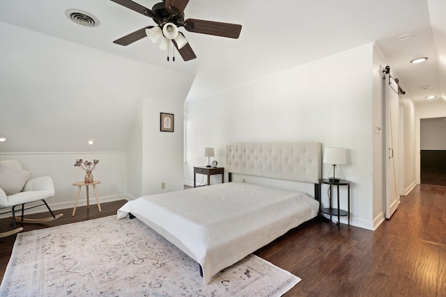 bedroom featuring lofted ceiling, a barn door, dark wood-type flooring, and ceiling fan