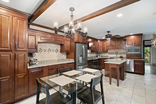 kitchen with decorative backsplash, a kitchen island, light stone countertops, decorative light fixtures, and appliances with stainless steel finishes