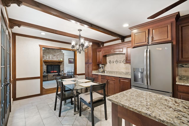 kitchen featuring stainless steel fridge, tasteful backsplash, light stone countertops, a brick fireplace, and pendant lighting