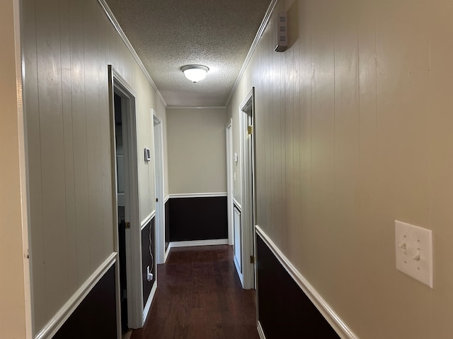 corridor with ornamental molding, dark wood-type flooring, a textured ceiling, and wood walls