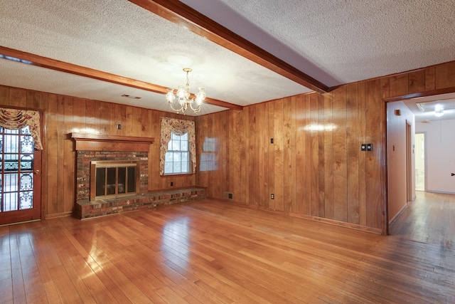 unfurnished living room featuring a fireplace, beam ceiling, hardwood / wood-style flooring, a chandelier, and wood walls