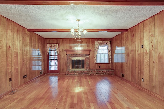 unfurnished living room featuring light hardwood / wood-style flooring, wooden walls, a brick fireplace, a notable chandelier, and a textured ceiling