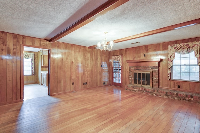 unfurnished living room with beam ceiling, a wealth of natural light, a fireplace, and light hardwood / wood-style floors