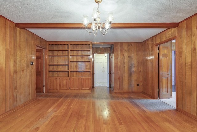 unfurnished dining area with beam ceiling, light wood-type flooring, a textured ceiling, and wooden walls