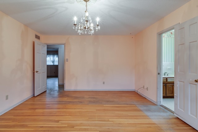 empty room with light hardwood / wood-style flooring and a chandelier