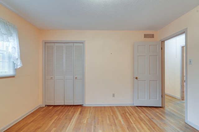 unfurnished bedroom featuring a textured ceiling, light wood-type flooring, and a closet