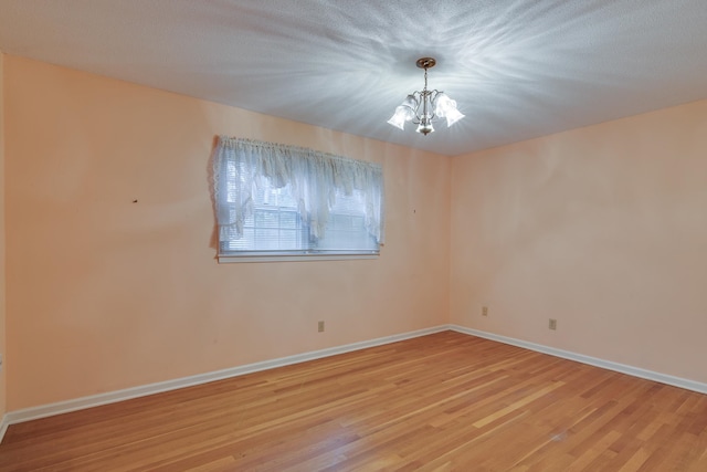 empty room featuring a chandelier, a textured ceiling, and light hardwood / wood-style flooring