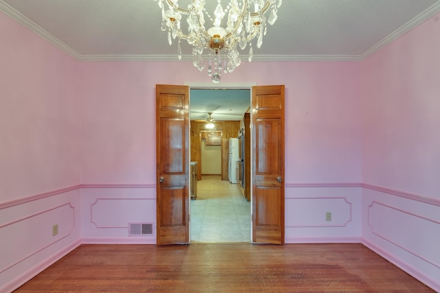 unfurnished room with hardwood / wood-style floors, an inviting chandelier, and crown molding