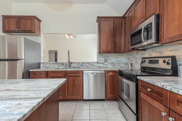 kitchen with appliances with stainless steel finishes, light tile patterned flooring, sink, light stone counters, and decorative backsplash