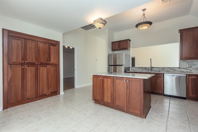 kitchen with light stone countertops, appliances with stainless steel finishes, sink, a center island, and decorative light fixtures