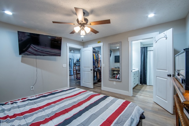 bedroom with a spacious closet, ensuite bath, a closet, ceiling fan, and light hardwood / wood-style flooring