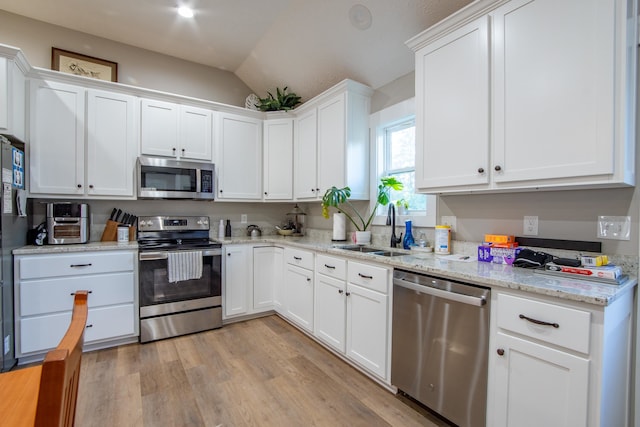 kitchen featuring sink, light hardwood / wood-style floors, stainless steel appliances, vaulted ceiling, and white cabinets