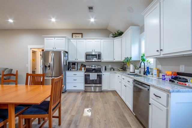 kitchen with white cabinetry, stainless steel appliances, sink, and vaulted ceiling