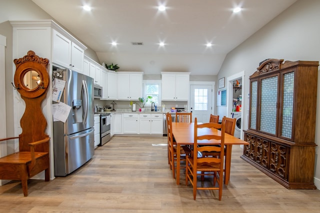 kitchen with washer / clothes dryer, appliances with stainless steel finishes, white cabinetry, light hardwood / wood-style floors, and vaulted ceiling