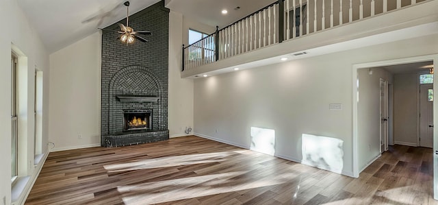 unfurnished living room featuring a healthy amount of sunlight, high vaulted ceiling, a fireplace, and hardwood / wood-style floors