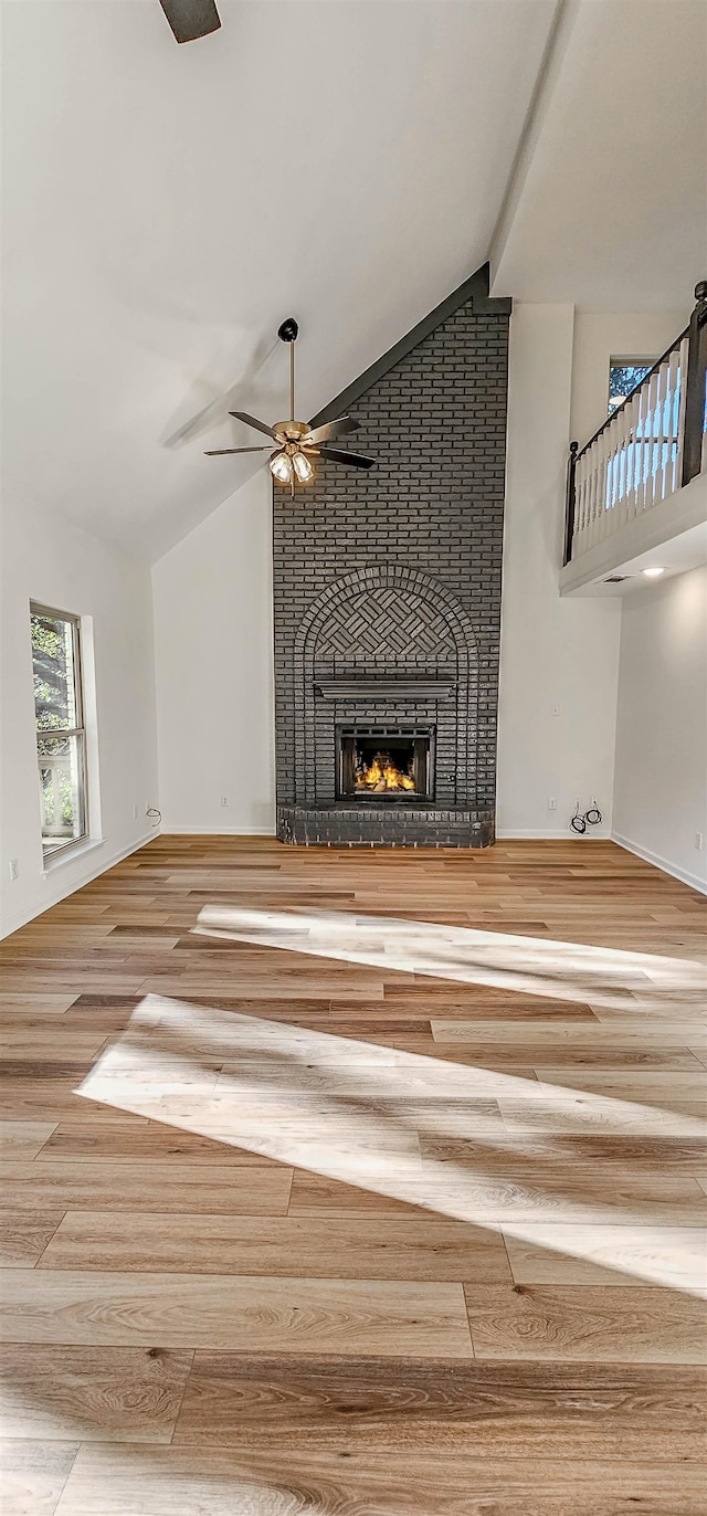 unfurnished living room featuring ceiling fan, high vaulted ceiling, wood-type flooring, and a fireplace