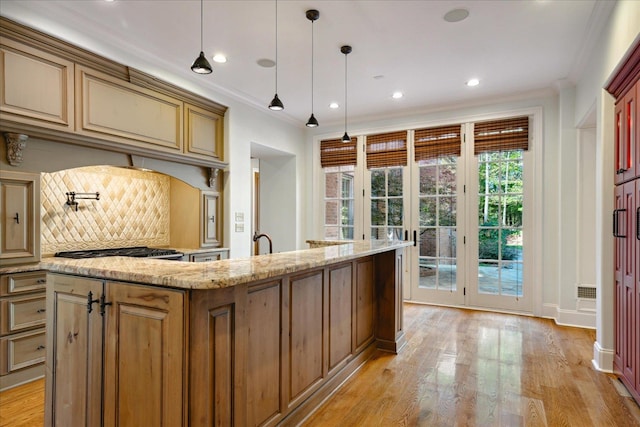 kitchen featuring a kitchen island with sink, light hardwood / wood-style flooring, hanging light fixtures, backsplash, and light stone countertops