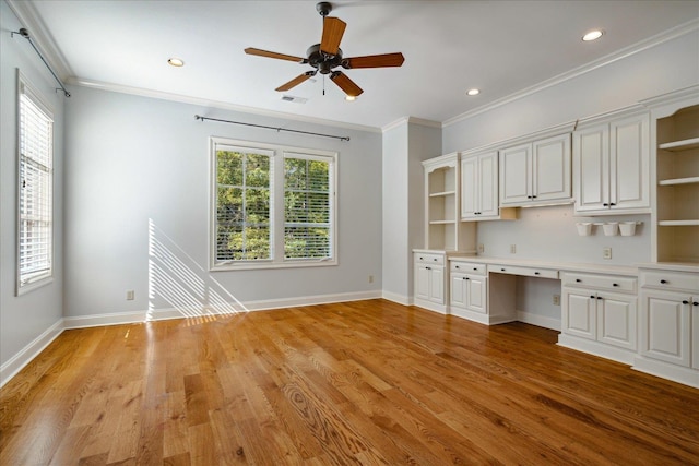 unfurnished office featuring light hardwood / wood-style floors, ornamental molding, built in desk, and ceiling fan