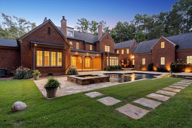 back house at dusk featuring a patio area and a lawn