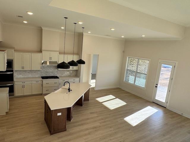 kitchen with pendant lighting, white cabinets, an island with sink, decorative backsplash, and high vaulted ceiling