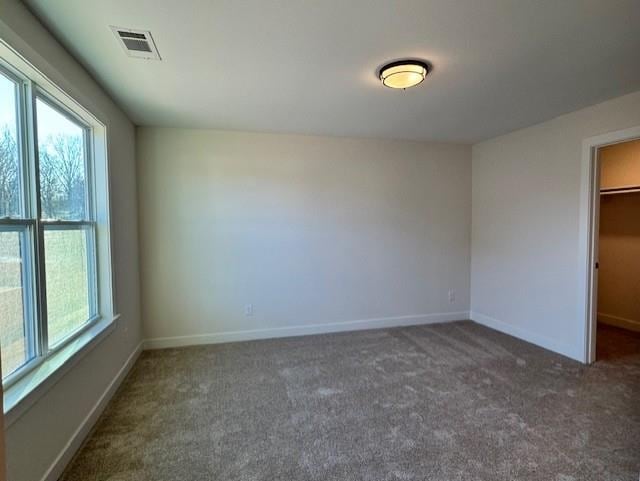 unfurnished bedroom with a walk in closet, a closet, and dark colored carpet