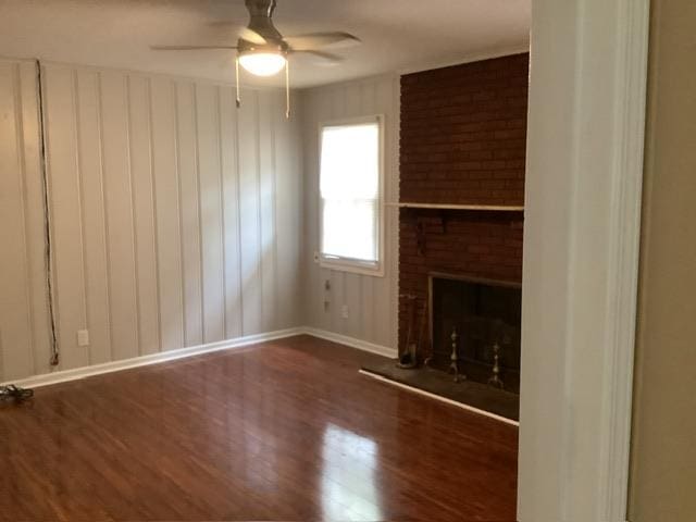 unfurnished living room featuring dark wood-type flooring, a brick fireplace, and ceiling fan