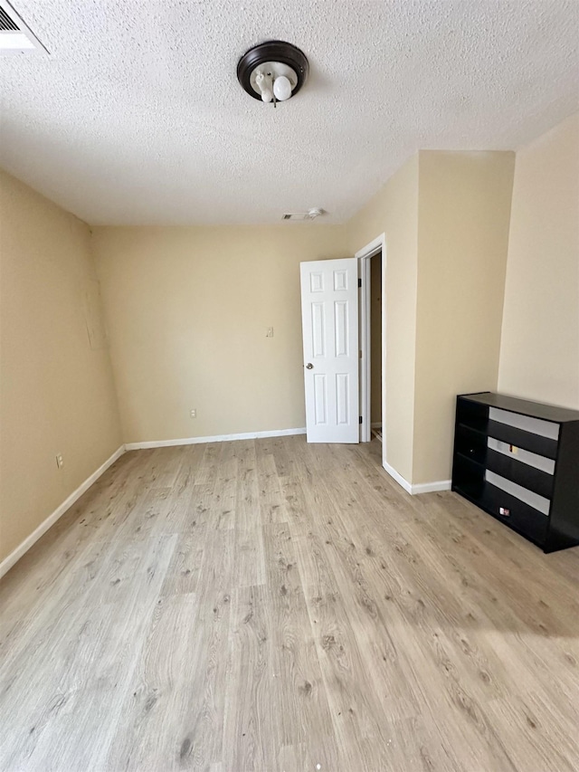 spare room featuring light wood-type flooring and a textured ceiling