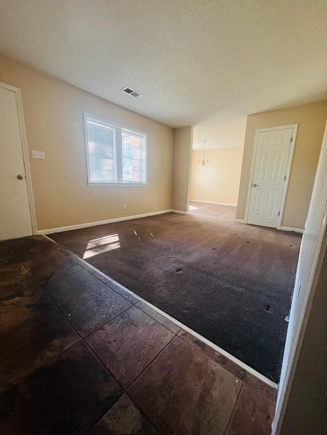 unfurnished room featuring a textured ceiling, an inviting chandelier, and dark colored carpet