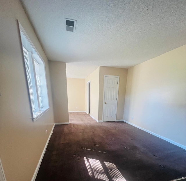 unfurnished room featuring a textured ceiling and dark colored carpet