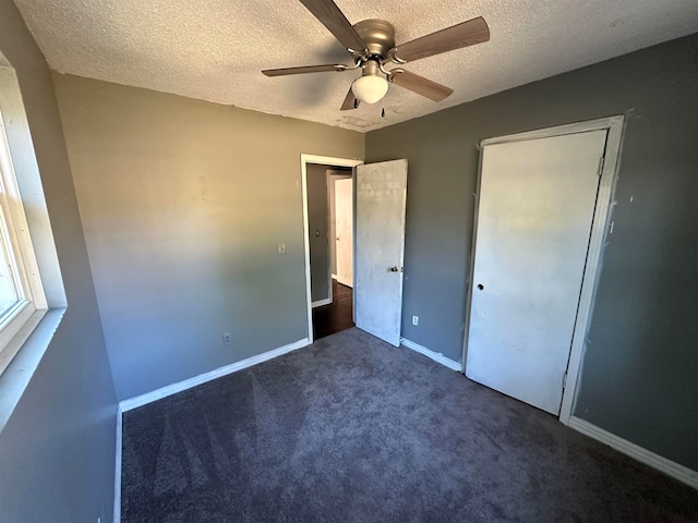 unfurnished bedroom with a closet, ceiling fan, a textured ceiling, and dark carpet