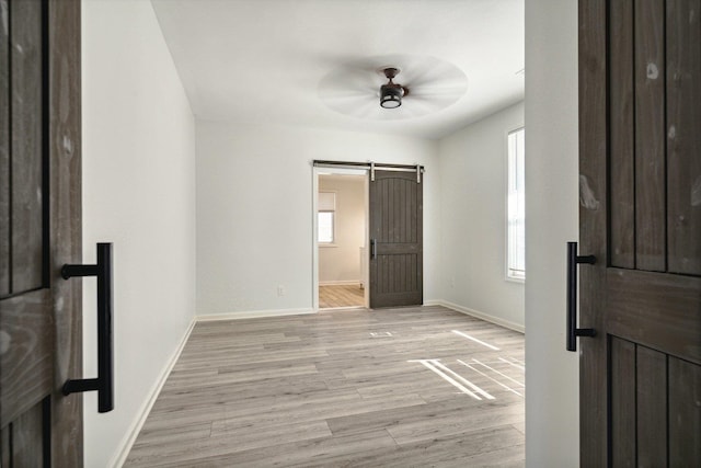 unfurnished bedroom with light hardwood / wood-style floors, ensuite bathroom, a barn door, and ceiling fan