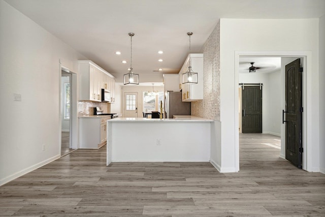 kitchen with kitchen peninsula, white cabinets, appliances with stainless steel finishes, a barn door, and decorative light fixtures