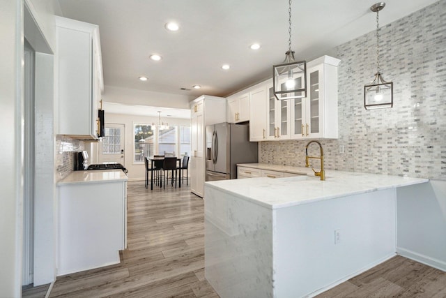 kitchen with kitchen peninsula, white cabinets, hanging light fixtures, and light wood-type flooring