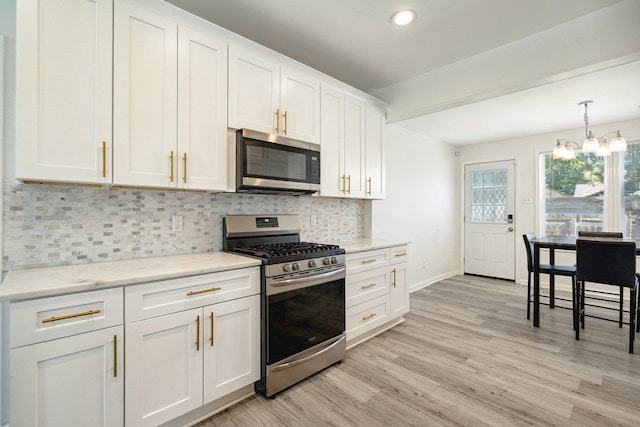 kitchen with decorative backsplash, stainless steel appliances, pendant lighting, white cabinetry, and light hardwood / wood-style floors