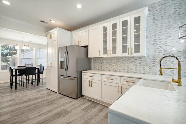 kitchen with white cabinets, stainless steel fridge with ice dispenser, light hardwood / wood-style floors, decorative light fixtures, and sink