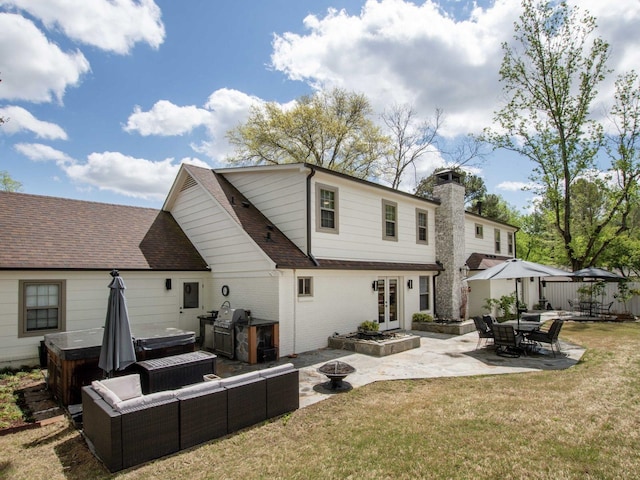 rear view of house with a hot tub, an outdoor fire pit, a patio area, and a lawn